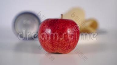 手把成熟的红苹果放在前景。 铝罐里有碳酸饮料和薯片，放在盘子里，不能集中精力吃